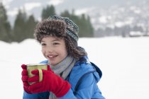 Glücklicher Junge trinkt heiße Schokolade im verschneiten Feld — Stockfoto