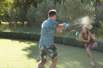 Кавказская пара играет с водяными пистолетами на заднем дворе — стоковое фото