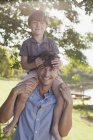 Батько носить усміхненого сина на плечах на березі озера — стокове фото