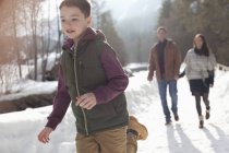Родители смотрят, как мальчик бежит по снежной полосе — стоковое фото