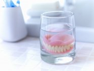 Primer plano de dentaduras postizas empapadas en un vaso de agua - foto de stock