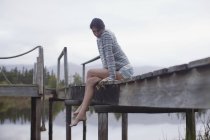Спокойная женщина, сидящая на краю дока над озером — стоковое фото