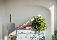 Easel with painting next to bureau with plants and supplies on patio — Stock Photo