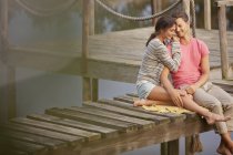 Affectionate couple sitting on dock over lake — Stock Photo