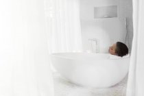 Женщина расслабляется в ванной в современной ванной комнате — стоковое фото
