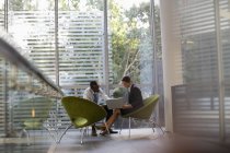 Бизнесмен и предпринимательница пользуются ноутбуком в лобби современного офиса — стоковое фото