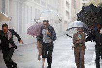 Энтузиасты бизнеса с зонтиками, бегущими по дождливой улице — стоковое фото