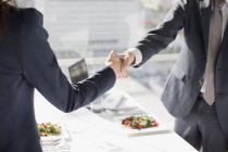 Empresário e empresária apertando as mãos à mesa com o almoço — Fotografia de Stock