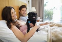 Couple relaxing with dog in bed at modern home — Stock Photo
