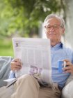 Man reading newspaper in porch swing — Stock Photo