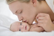 Mother kissing newborn baby on bed — Stock Photo