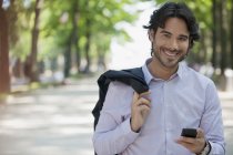 Portrait of smiling man holding cell phone in park — Stock Photo