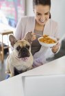 Mujer comiendo cereal con perro en regazo - foto de stock