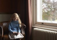 Девушка просматривает цифровой планшет в кресле дома — стоковое фото