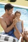 Father applying sunscreen to daughter's nose by swimming pool — Stock Photo
