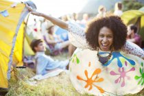 Portrait of playful woman laying on inflatable chair outside tents at music festival — Stock Photo