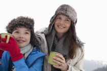 Счастливые мать и сын в меховых шапках пьют горячий шоколад — стоковое фото