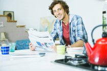 Молодий щасливий чоловік читає газету на кухні — стокове фото