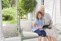 Woman and granddaughter reading on porch swing — Stock Photo