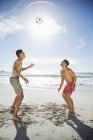 Homens em troncos de natação dirigindo bola de futebol na praia — Fotografia de Stock