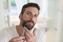 Мужчина стрижет бороду в ванной комнате — стоковое фото