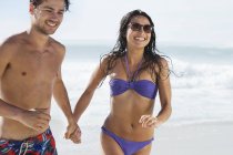 Happy couple holding hands and running on beach — Stock Photo
