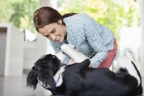 Smiling woman playing with dog at modern home — Stock Photo