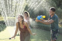 Amigos brincando com armas de água no aspersor no quintal — Fotografia de Stock