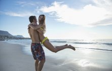 Glückliches Paar, das sich am Strand umarmt und dreht — Stockfoto