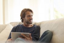 Junger attraktiver Mann nutzt Tablet-Computer auf dem Sofa — Stockfoto