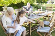Menina pedindo para animal de estimação gato à mesa ao ar livre — Fotografia de Stock