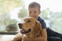 Lächelnder Junge umarmt Hund drinnen — Stockfoto
