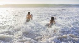 Heureux couple caucasien surf dans l'océan — Photo de stock