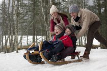 Happy family sledding in snowy woods — Stock Photo