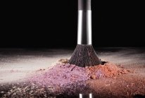 Makeup brush dipping into multicolor blush splatter — Stock Photo