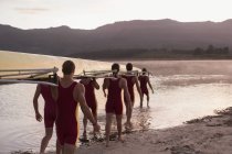 Rowing team carrying scull into lake at dawn — Stock Photo