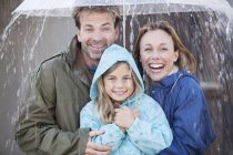 Портрет восторженной семьи под зонтиком под ливнем — стоковое фото