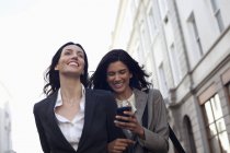 Mensajería de texto de empresarias felices con teléfono celular - foto de stock