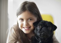 Улыбающаяся девушка держит собаку в современном доме — стоковое фото