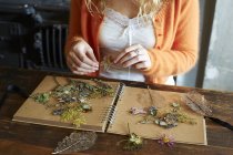 Frau arrangiert getrocknete Blumen und Kräuter auf Notizbuch — Stockfoto