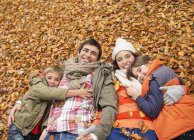 Família sorrindo que põe em folhas de outono — Fotografia de Stock