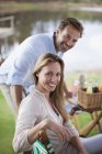 Retrato de pareja sonriente disfrutando de un picnic a orillas del lago - foto de stock