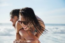 Homme portant femme enthousiaste sur la plage — Photo de stock