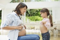 Mädchen und schwangere Mutter vergleichen Bäuche — Stockfoto