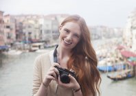 Retrato de una mujer sonriente sosteniendo una cámara digital en el paseo marítimo de Venecia - foto de stock