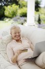Senior mulher compras on-line no sofá pátio — Fotografia de Stock