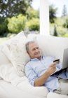 Homem caucasiano sênior compras on-line no sofá pátio — Fotografia de Stock