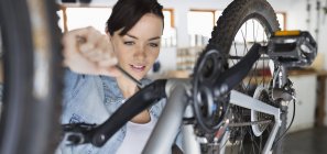 Skillful caucasian woman working on bicycle in shop — Stock Photo