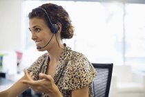 Mujer de negocios hablando en auriculares en el escritorio en la oficina moderna - foto de stock