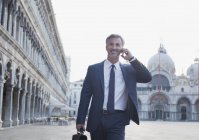 Lächelnder Geschäftsmann, der mit dem Handy telefoniert und über den Markusplatz in Venedig läuft — Stockfoto